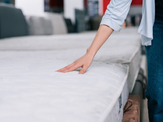 partial view of woman touching orthopedic mattress in furniture shop